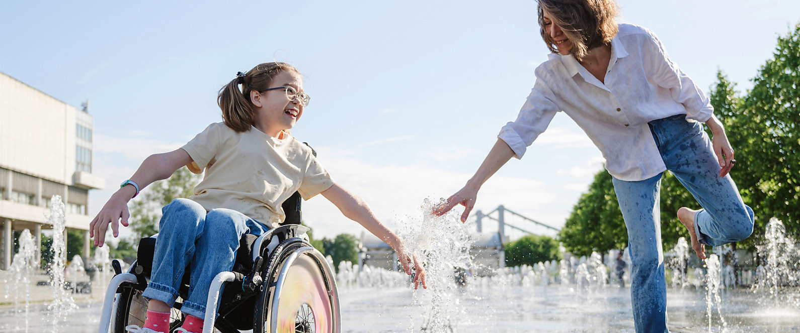 Mädchen im Rollstuhl spielt mit einer Frau in einem Springbrunnen