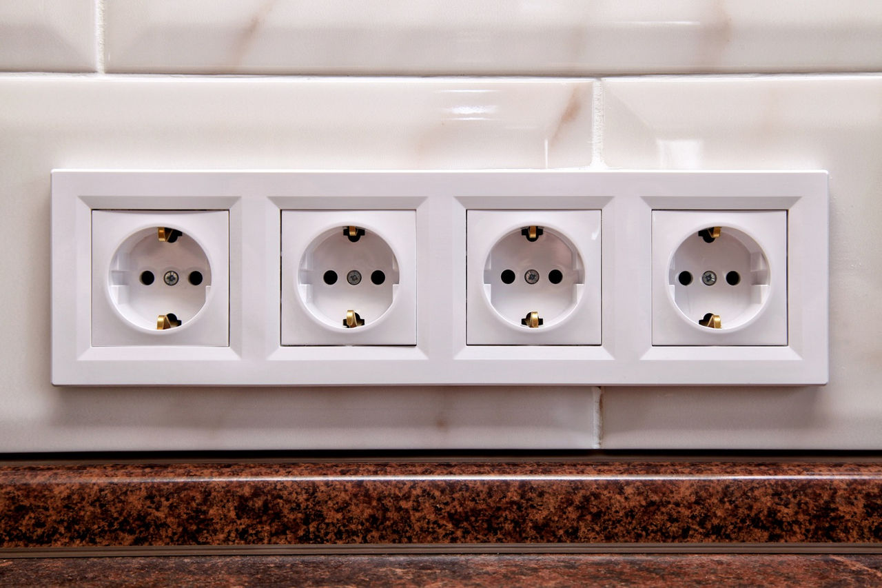 Four electrical power sockets on a kitchen tile wall