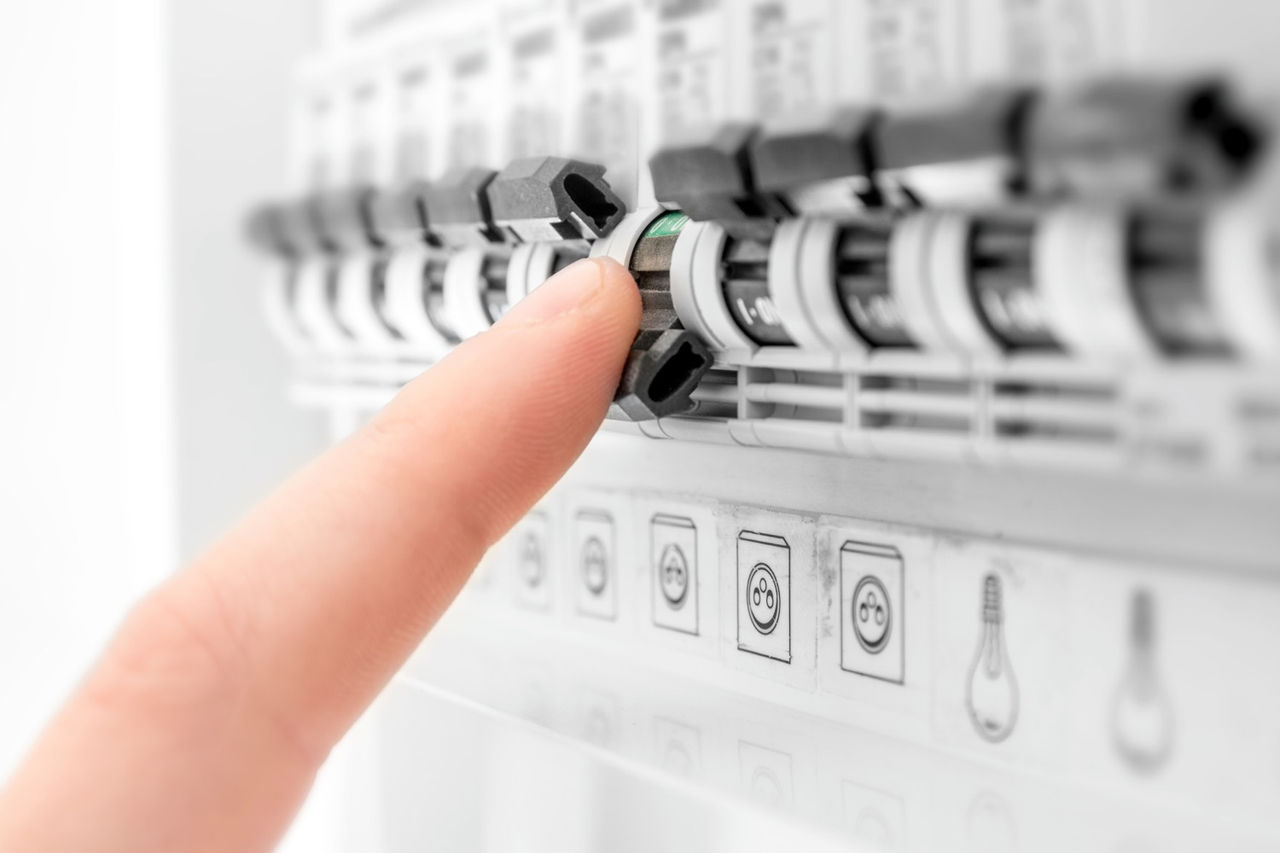 A human hand is cutting out, turning OFF a circuit breaker fuse box switch. Electrical cabinet, open, with electrical circuit breaker. Selective focus on the finger human hand and button of the circuit breaker (ON-OFF). Side view in selective focus of unrecognizable person.