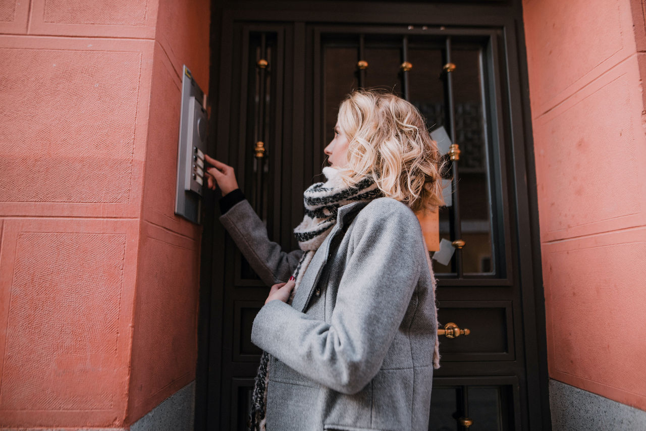 A woman ringing an apartment bell at the main entrance of a building