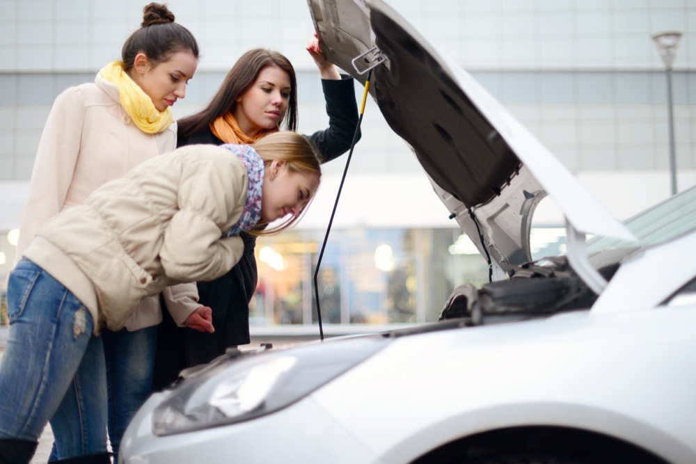 Three women look under the hood of a broken car