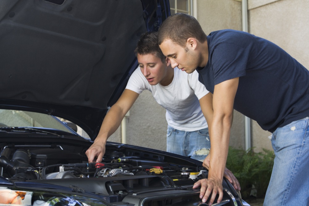 Two young man working on the engine of a car, repairing or maintaining machinery under the hood.