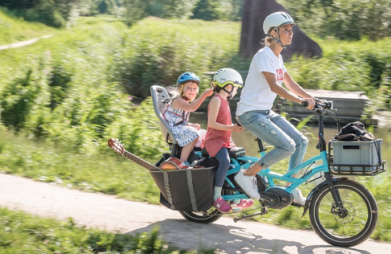 Mutter auf Fahrrad mit 2 Kindern, die hinter ihr am Fahrrad sitzen