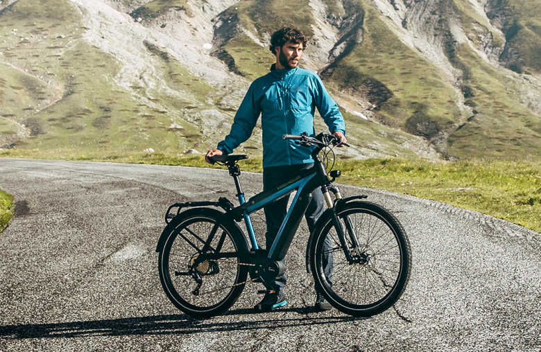 Person mit Windjacke neben blauem Fahrrad in Natur
